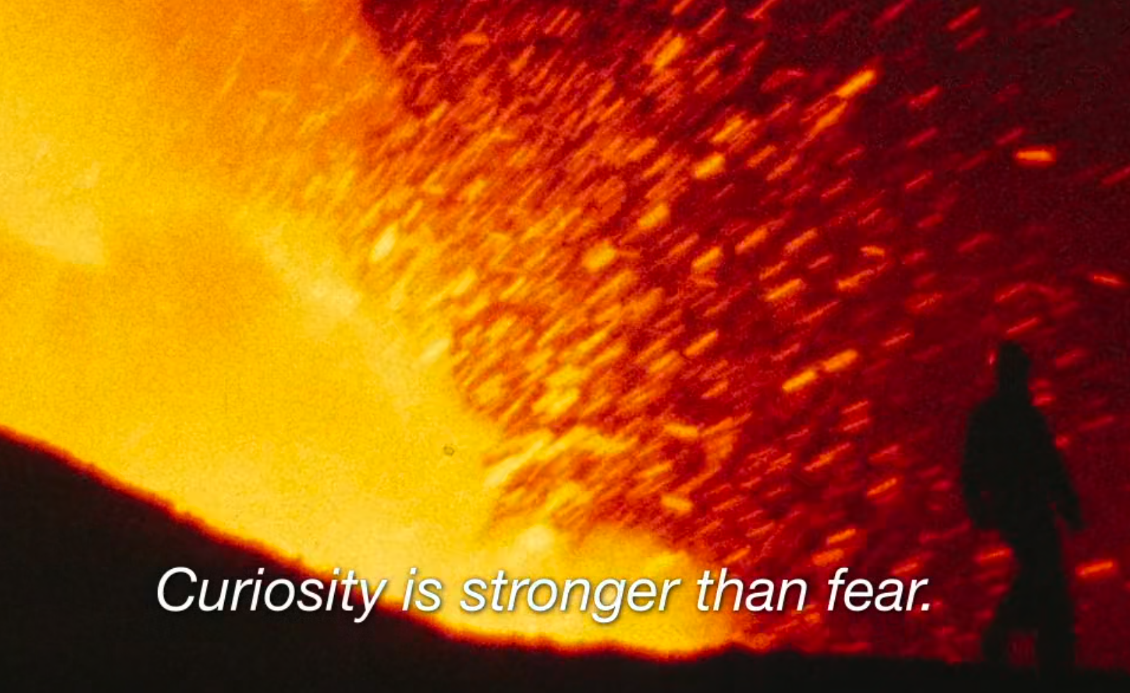 lava wave splashing, silhouetting a person walking along the mouth of the active volcano with the subtitle 'curiousity is stronger than fear'